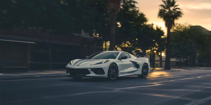 A white Chevrolet Corvette Stingray speeding on a city street at sunset.