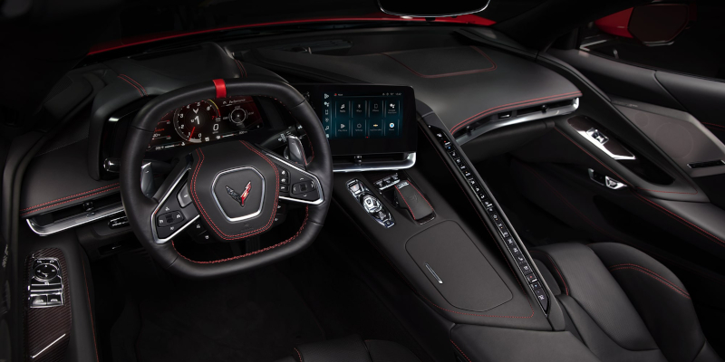 Interior of a Chevrolet Corvette Stingray featuring a digital dashboard, touchscreen, red-stitched leather, and driver-focused controls.