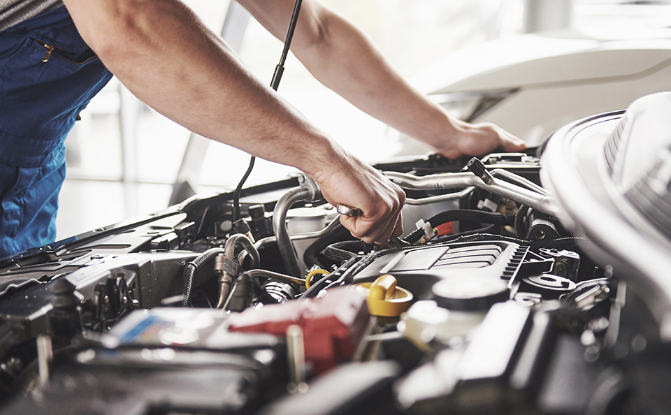 A close-up of a mechanic's hands using a wrench to work on a car engine under an open hood.