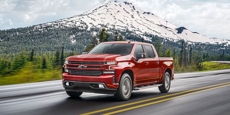 Red Chevy Silverado 1500 driving on road with snowy mountains behind