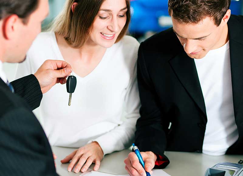 couple at dealership signing paperwork, salesman handing them car key