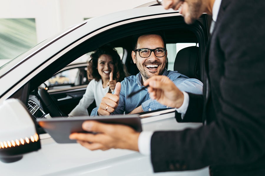 couple in car, man giving thumbs up to salesman