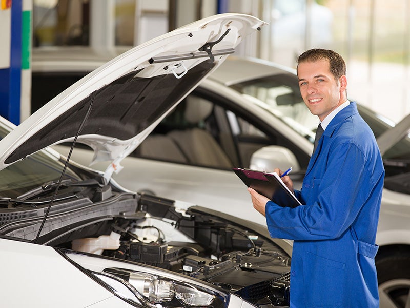 service manager holding clipboard standing in front of car with hood open